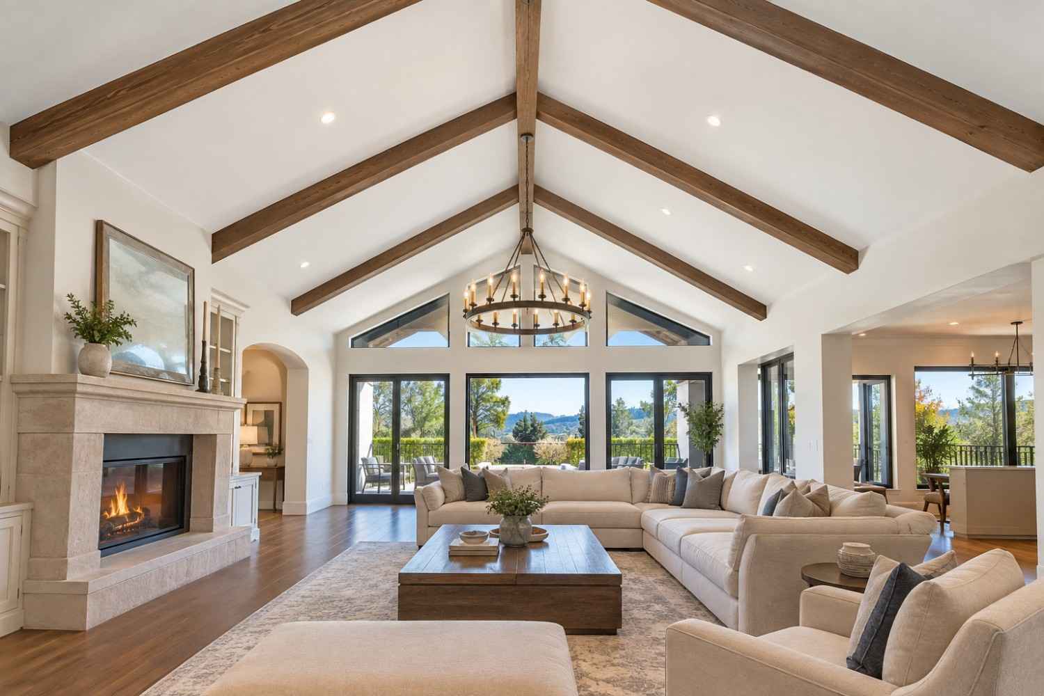Luxury living room with freshly painted white vaulted ceiling, exposed wood beams, stone fireplace, modern furnishings, hardwood flooring, and expansive windows overlooking a scenic California landscape.
